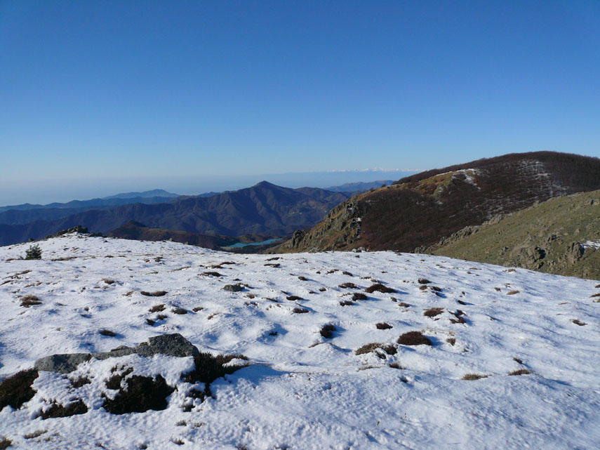 Ad ovest, in lontananza, appaiono le Alpi Liguri. Al centro della foto, piccolo ed azzurro, il Lago di Giacopiane