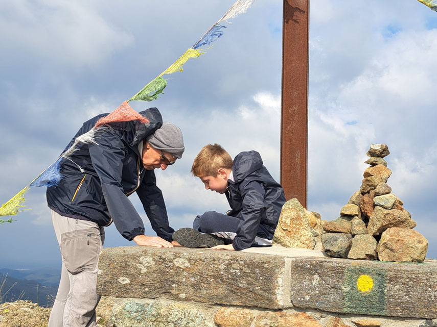 Le bandiere di preghiera colorate sventolano sulle teste di nonno e nipote mentre cercano di decifrare le scritte sul dischetto metallico del punto trigonometrico murato nel 1935 sul basamento della croce